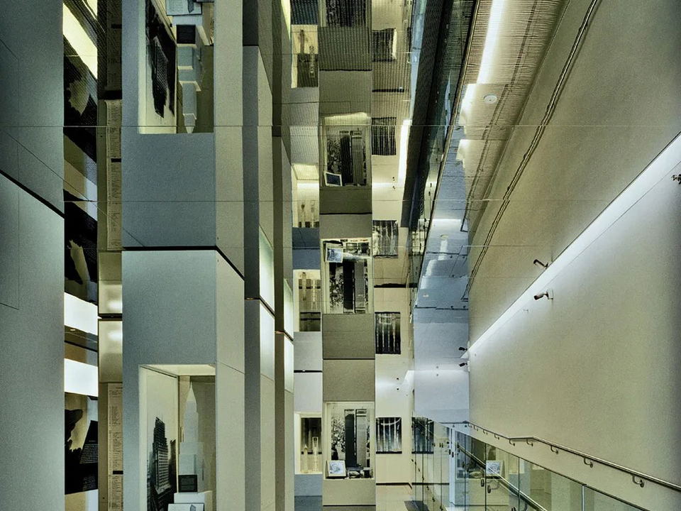 A dramatically mirrored multi-story interior corridor with reflective steel floors and ceilings, exhibition panels on the walls, and glass railings.