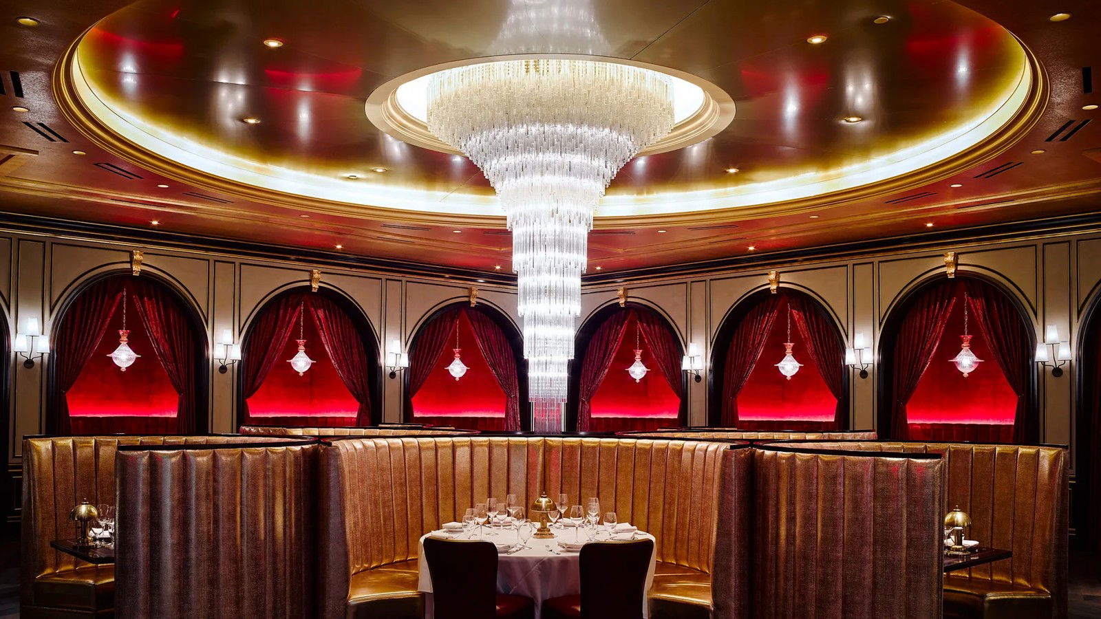 An opulent dining room with gold leather booths, arched alcoves with red velvet curtains, crystal pendant lights, and a large tiered crystal