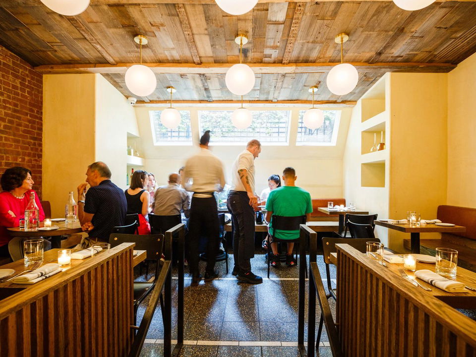 Interior of a restaurant with wooden tables, pendant lights, and diners.