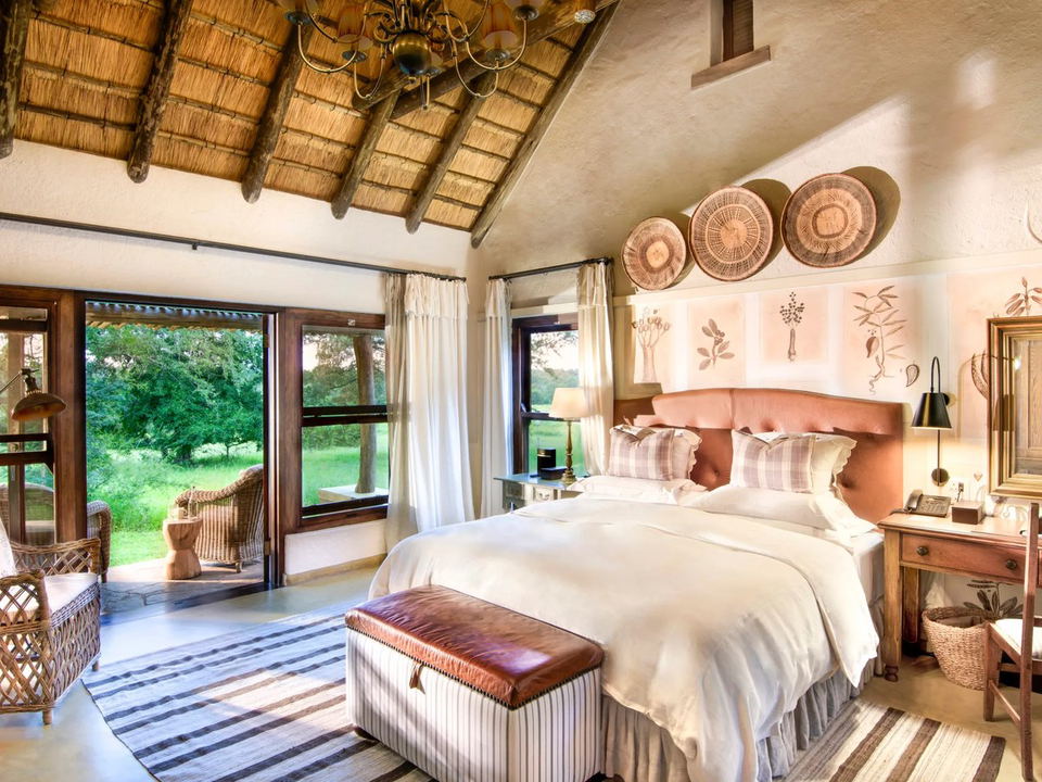 Singita offers a luxurious safari lodge experience with a thatched ceiling, wicker furniture, and lush bush views.