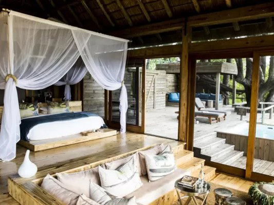 A luxury safari tent interior at Vumbura Plains Camp with a four-poster bed, lounge seating, and an open deck with a plunge pool.