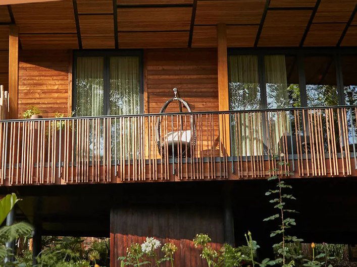A contemporary wood-clad building with large windows and a metal-railed deck, surrounded by tropical plants and landscaping.