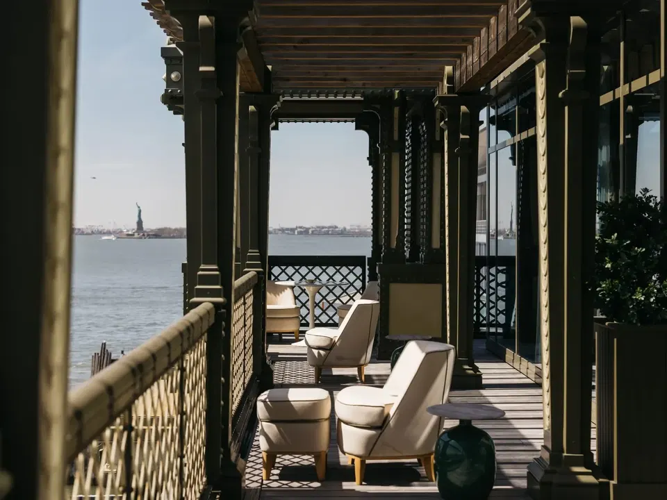 Balcony view with chairs overlooking water and the Statue of Liberty.