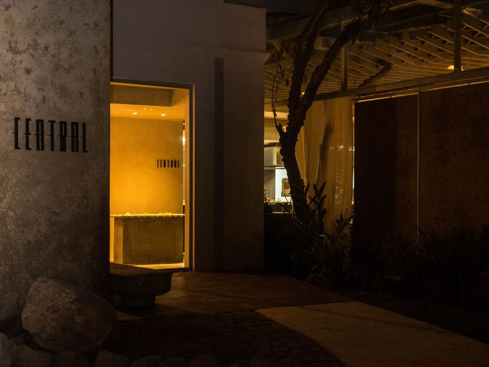 The exterior of Central restaurant at night, showing a textured concrete wall with "CENTRAL" signage and a warmly lit doorway.