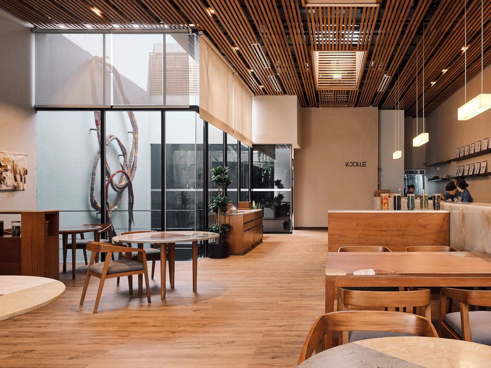 A minimalist dining room at Kjolle in Barranco, Lima, featuring wood slat ceilings, natural wood furniture, and large glass walls.