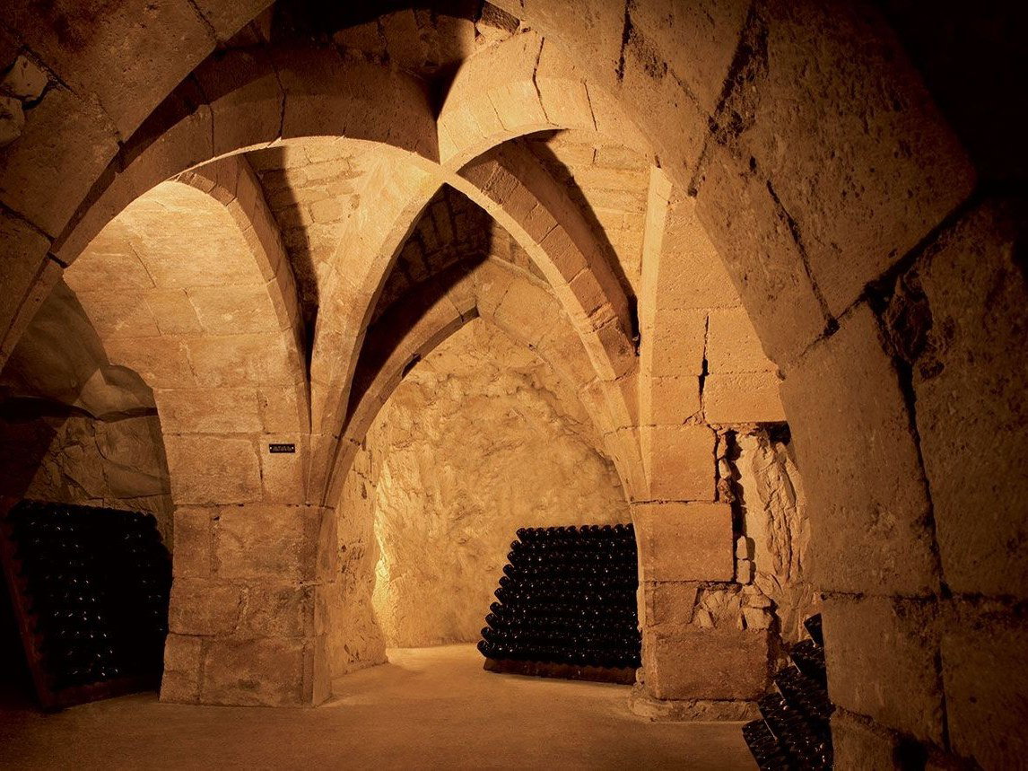 Champagne Taittinger's Reims cellars, a beautifully lit underground chalk cellar with Gothic ribbed vaulting and stacked bottles.