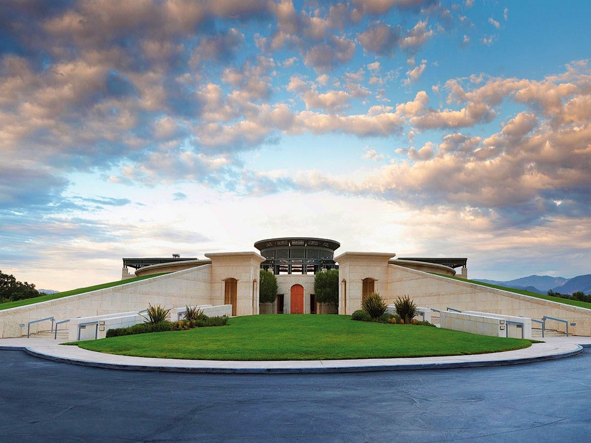 Exterior wide shot of the Opus One Winery building in Oakville, Napa Valley, showing its distinctive low-profile limestone facade with a