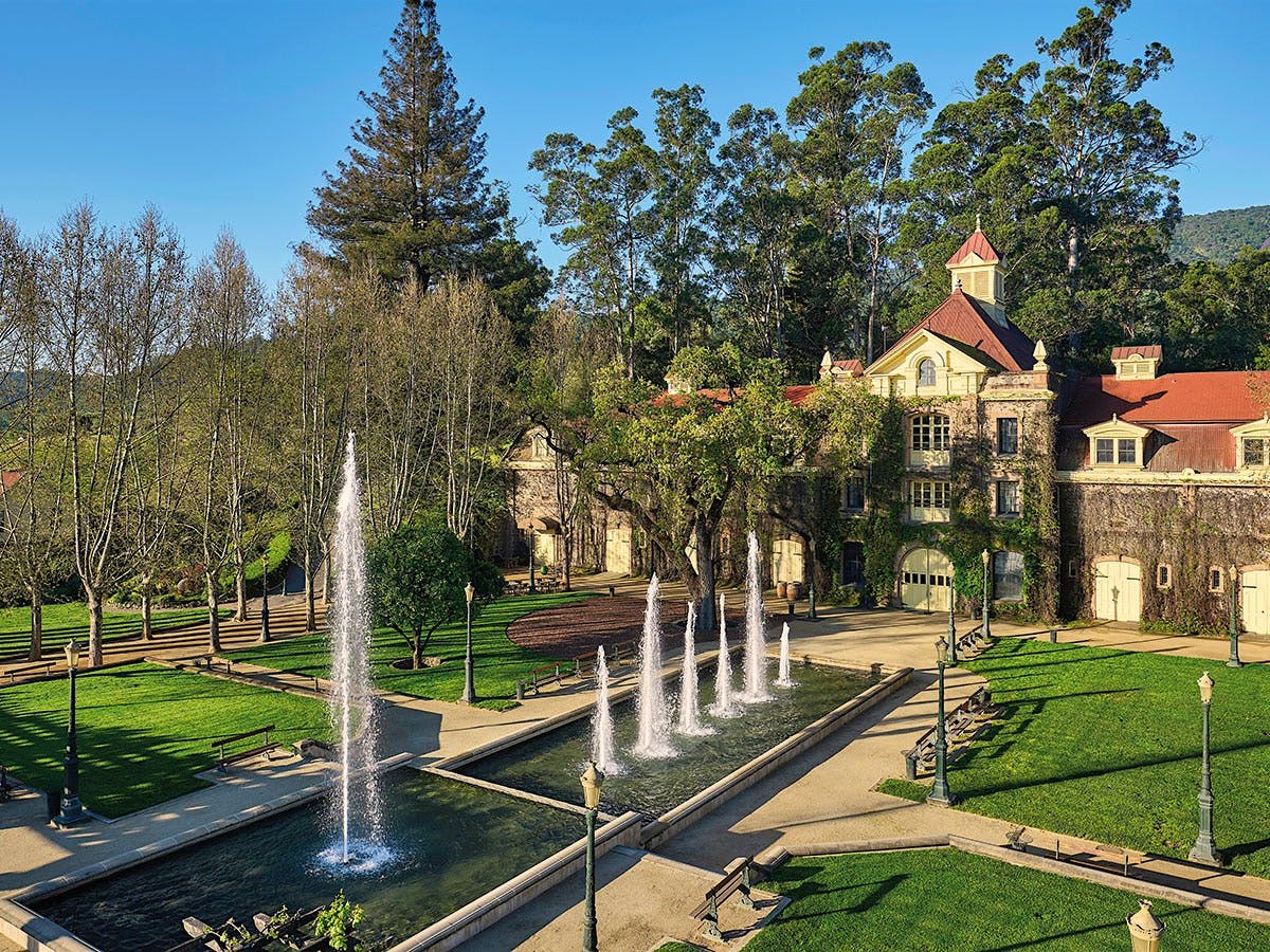 An aerial view of Inglenook's historic stone château with a red roof, ivy-covered walls, and a formal reflecting pool with fountains.