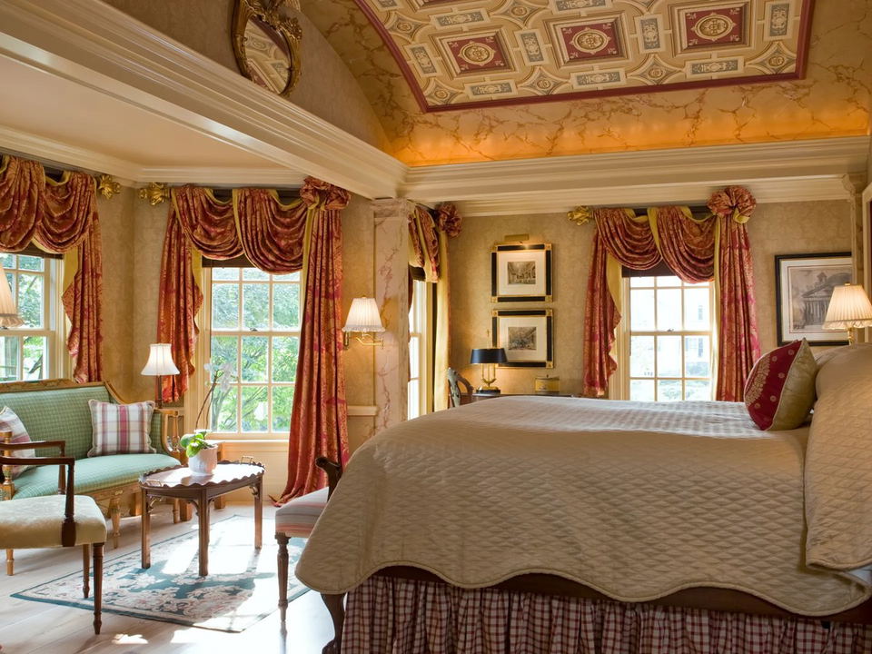 Luxurious guest room with ornate decor, large windows, and seating area.