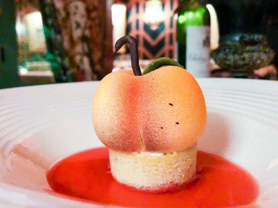 Dessert resembling a peach on a plate with raspberry sauce.