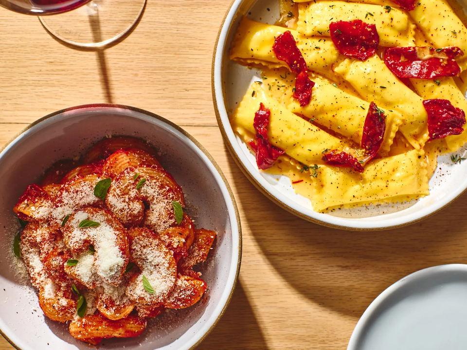Two pasta dishes, one with large ravioli and sun-dried tomatoes, the other with tomato sauce and grated cheese.