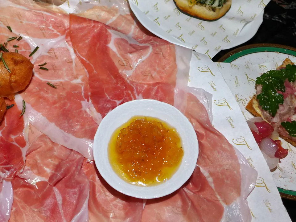 A Torrisi tasting menu course with prosciutto, orange marmalade, a bruschetta with minced clams and greens, and a crostino with head cheese.
