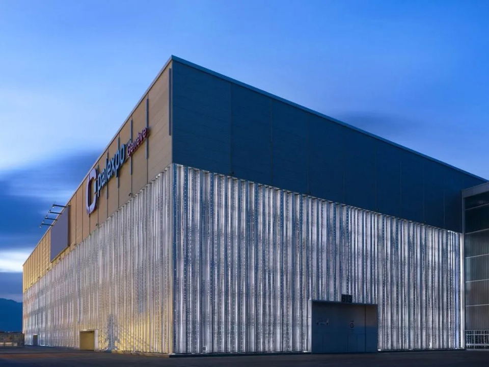 Exterior shot of Palexpo Geneva at dusk, featuring a modern building with a corrugated metallic facade and 'Palexpo Genève' signage.