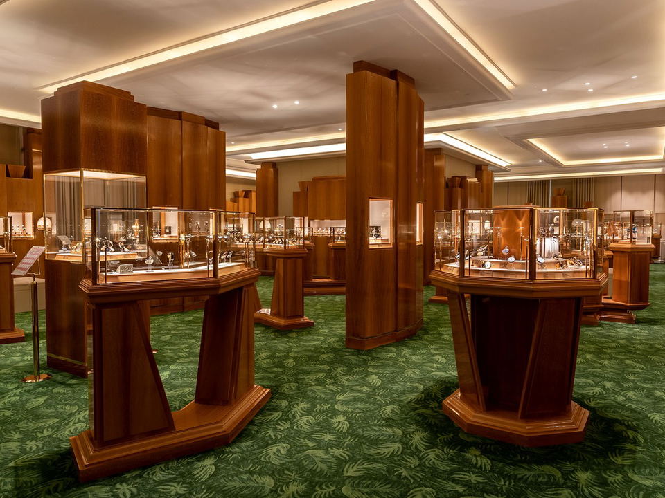 Interior of the Patek Philippe Museum in Geneva, showing numerous wooden display cases with glass vitrines containing watches, on a green patterned.