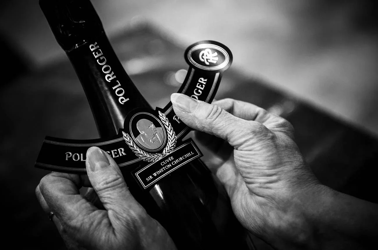 Hands holding a bottle of Pol Roger Cuvée Sir Winston Churchill in black and white.