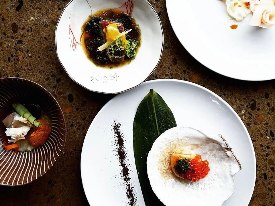 Overhead view of four plated omakase courses, including nigiri, sashimi, and garnished dishes, on white plates.
