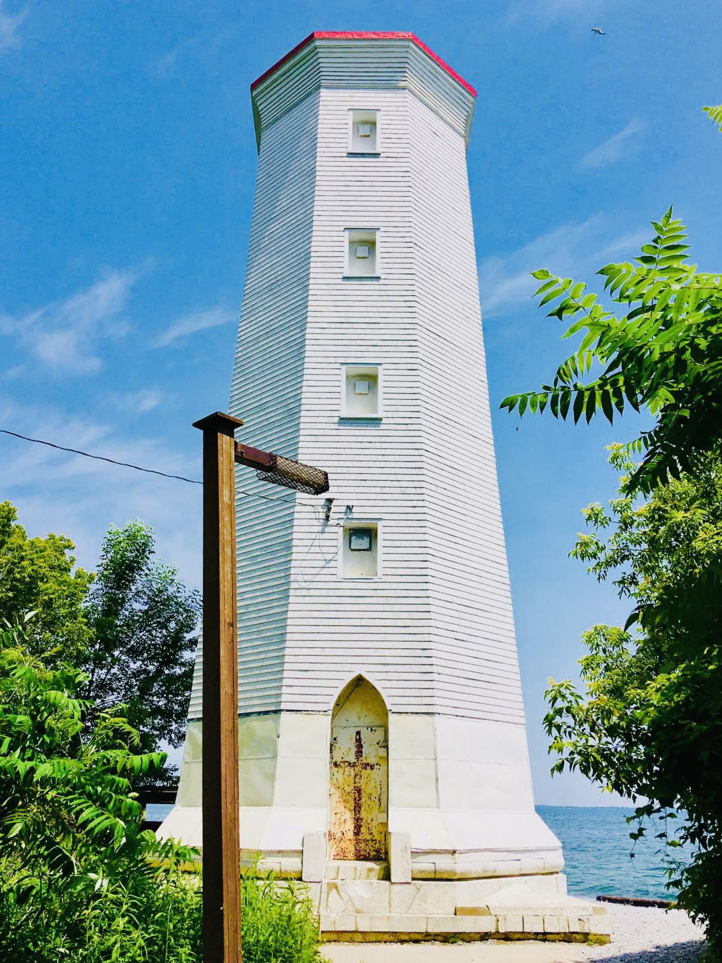 White lighthouse with red roof near water and greenery.
