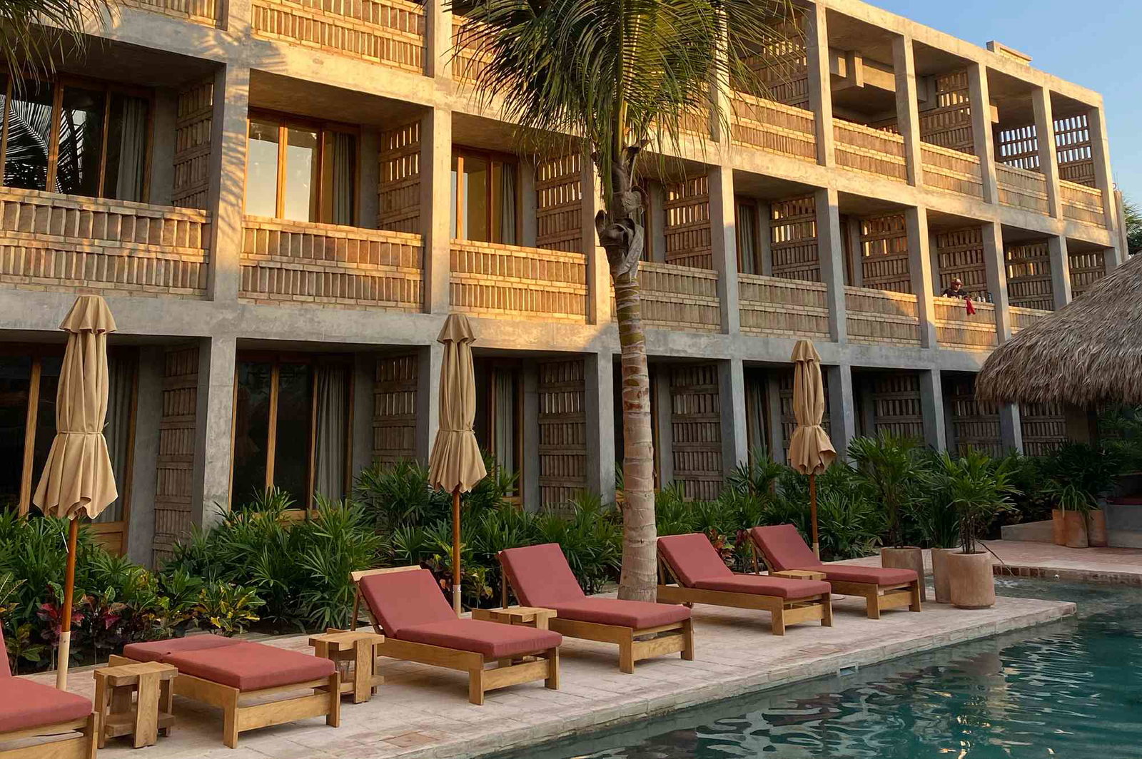 Hotel Humano, a multi-story building with balconies, a palm tree, and lounge chairs by a swimming pool.