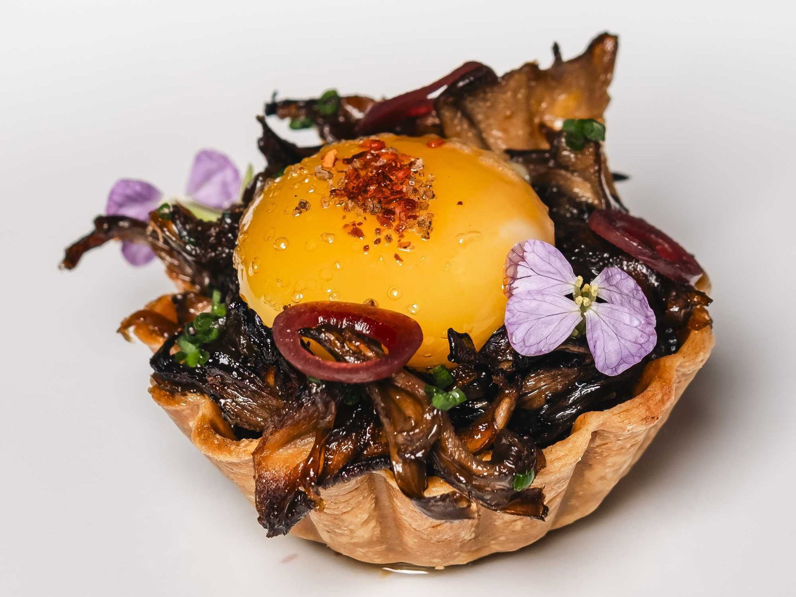 The Chef’s Menu: Winter 2024 Edition features a vibrant yellow sphere topped with red flakes and delicate purple flowers.