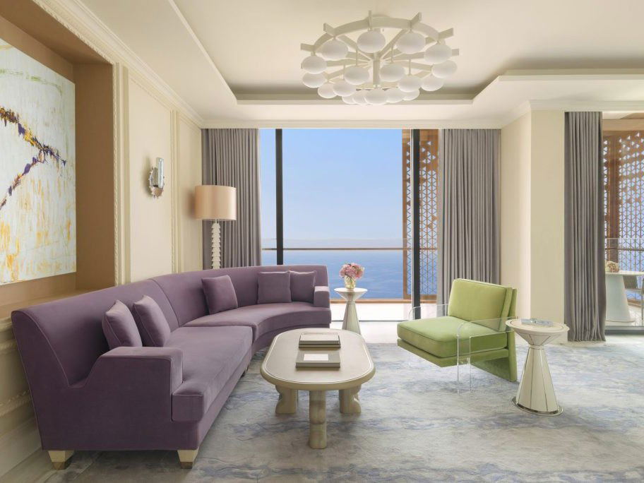 A luxurious living room with a curved purple sofa, a light green armchair, and a coffee table, overlooking the ocean.