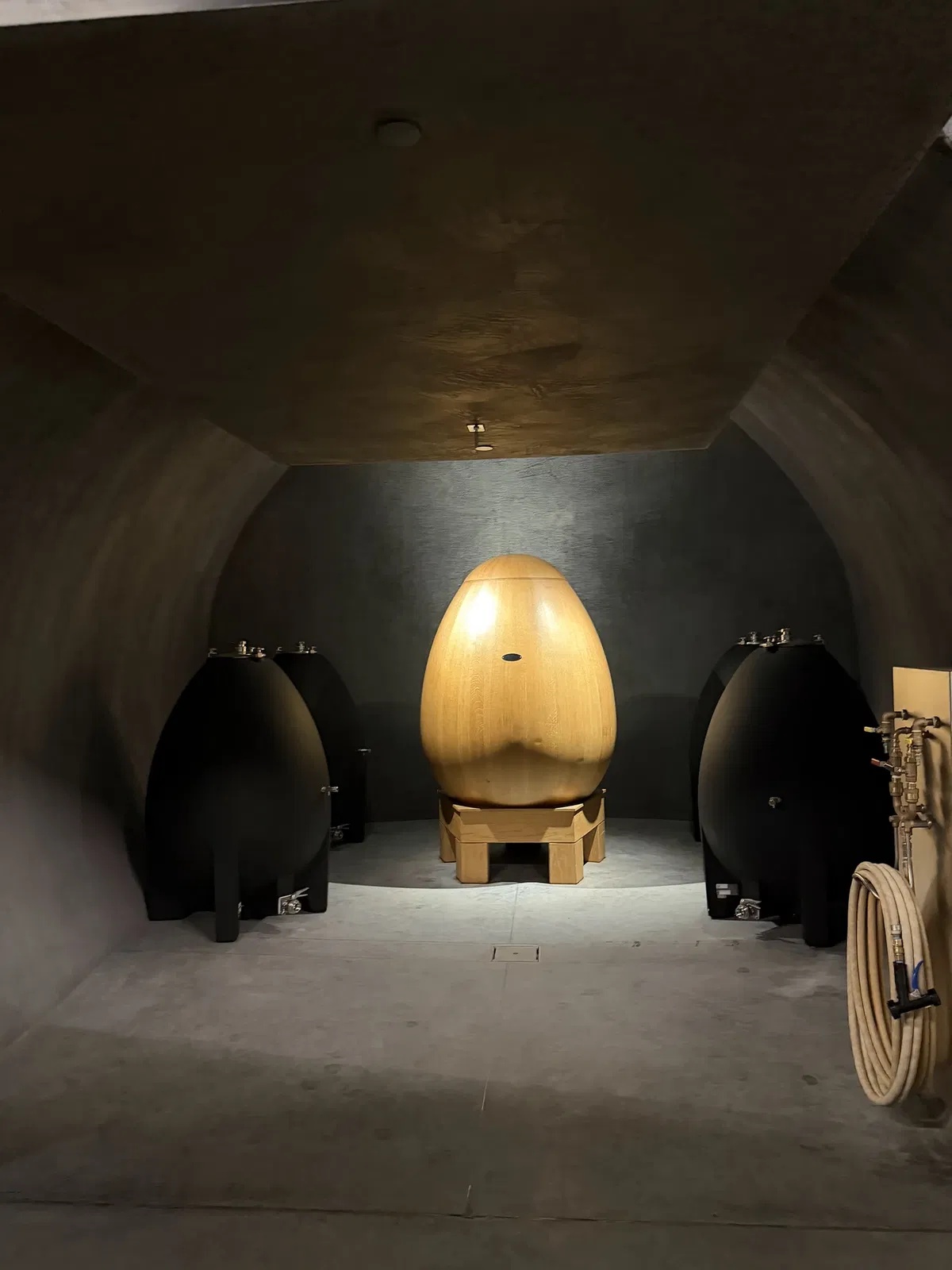 Large illuminated wooden ovum surrounded by concrete and clay wine vessels at Realm Houyi
