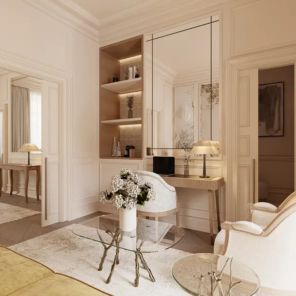 An elegant hotel suite interior with cream and beige tones, featuring a vanity desk with mirror, built-in shelving with lighting, and views.