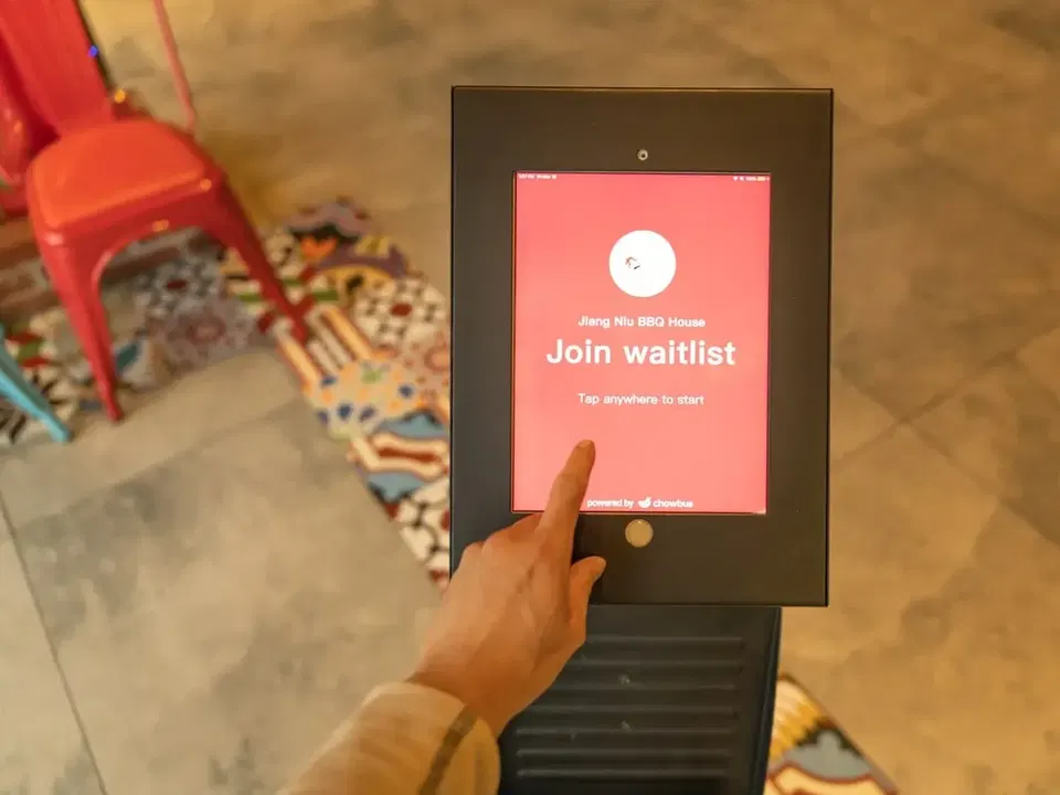 Digital waitlist kiosk with colorful chairs and patterned floor tiles.