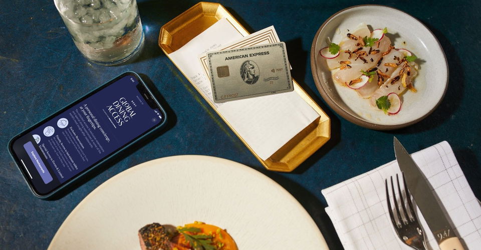 Overhead shot of a dining table showing an American Express Platinum card on a check tray, an iPhone displaying Resy's Global Dining Access interface.
