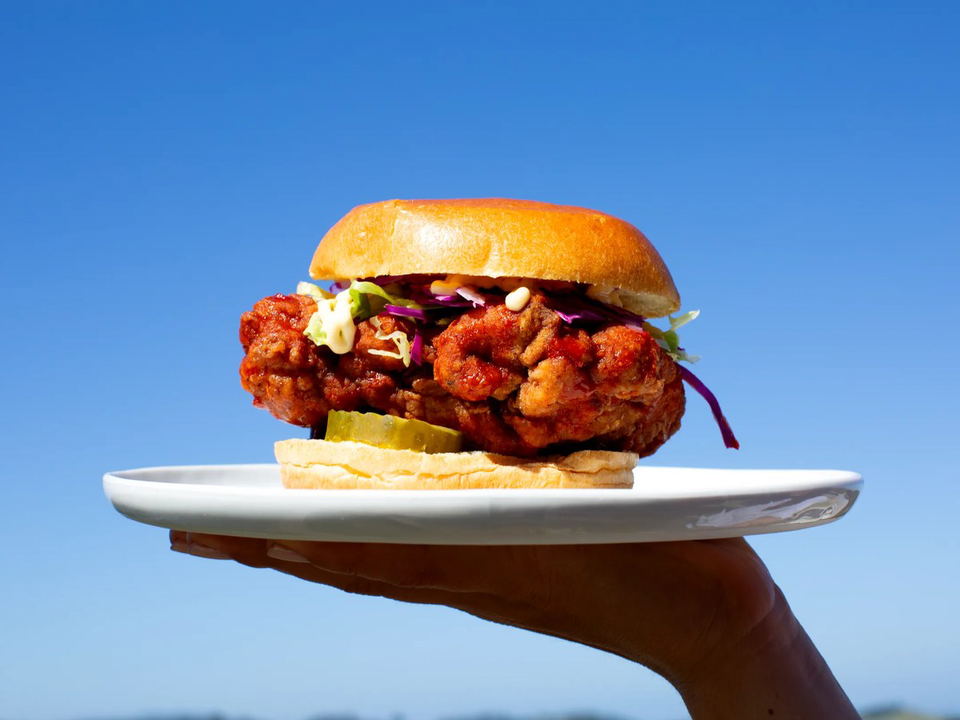 Saam San Francisco's tiger prawn sandwich, served with pickles, slaw, and sauce on a brioche bun.