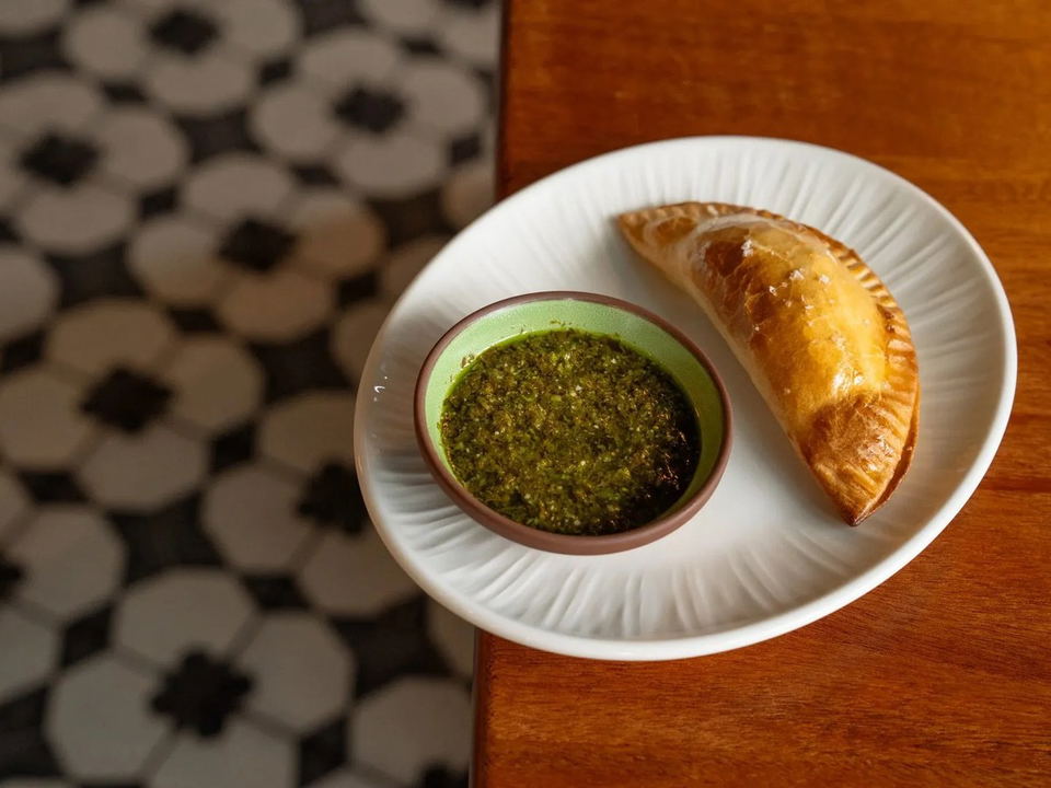 Sazanami serves a golden-brown empanada with vibrant green chimichurri sauce.