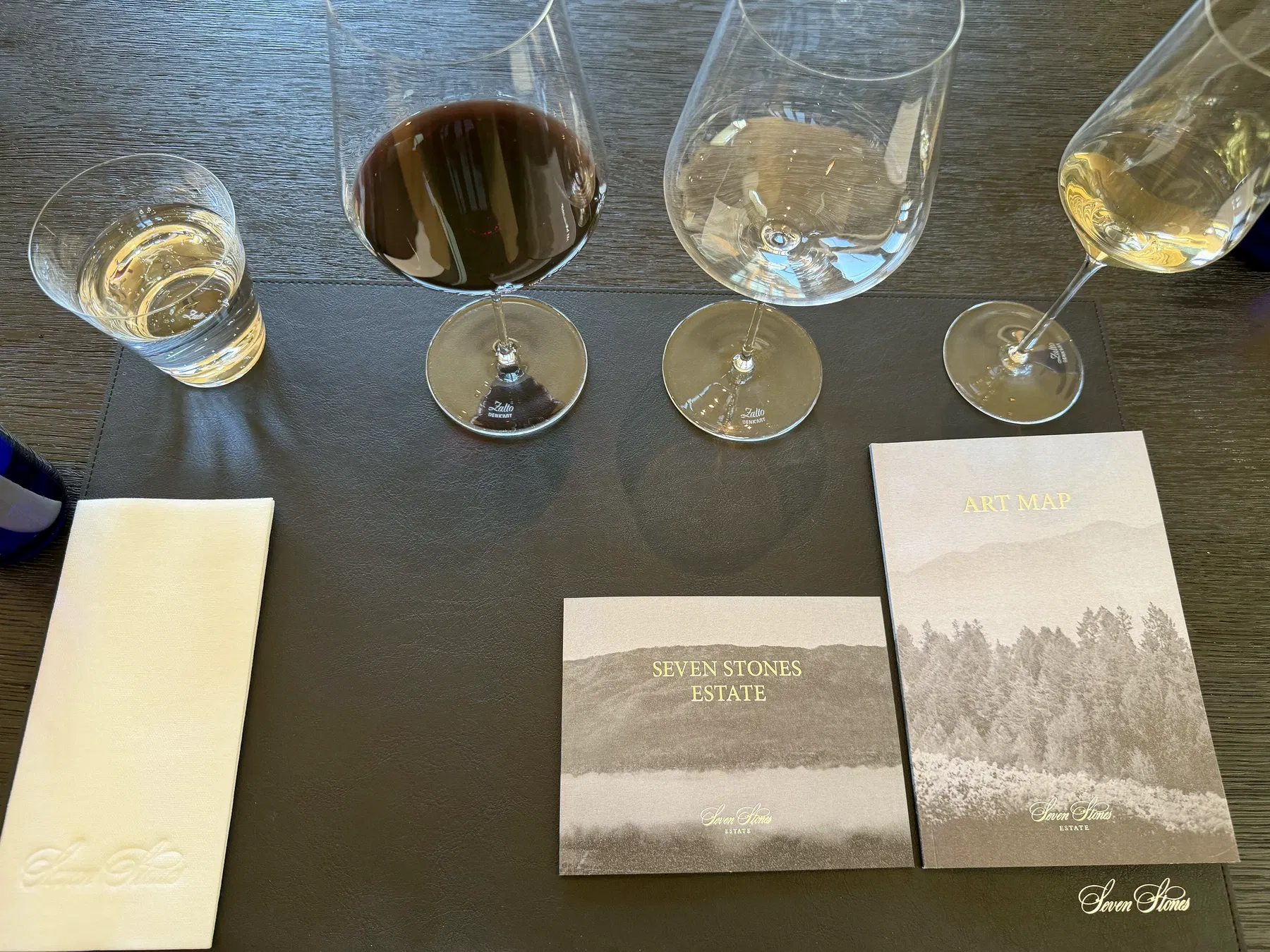 Seven Stones Estate art map and booklet beside wine glasses on the tasting table