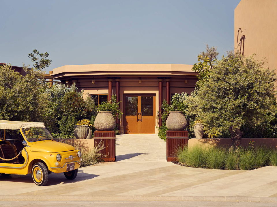 The exterior entrance of Gigi Rigolatto at J1 Beach Dubai, featuring a yellow Fiat 500, lush greenery, and large stone urns.