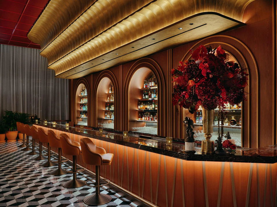 An opulent bar interior with arched niches displaying liquor bottles, warm amber lighting, leather bar stools, a dark marble counter, and a dramatic