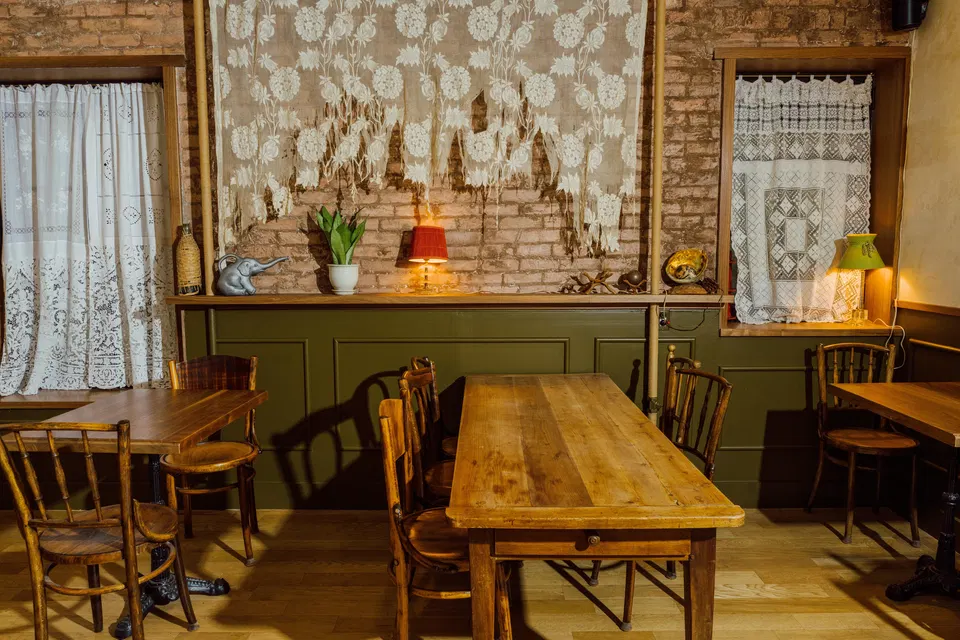 The interior of Somssi NYC restaurant, featuring wooden tables and chairs, decorative curtains, and a brick wall.