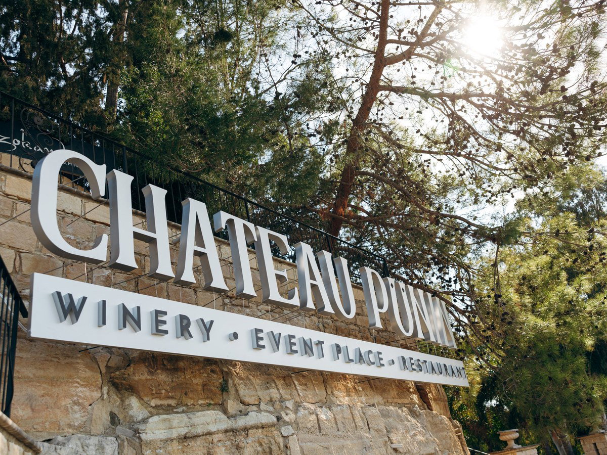 A winery entrance with a stone wall and trees, hinting at the ideal conditions for a prized vintage.