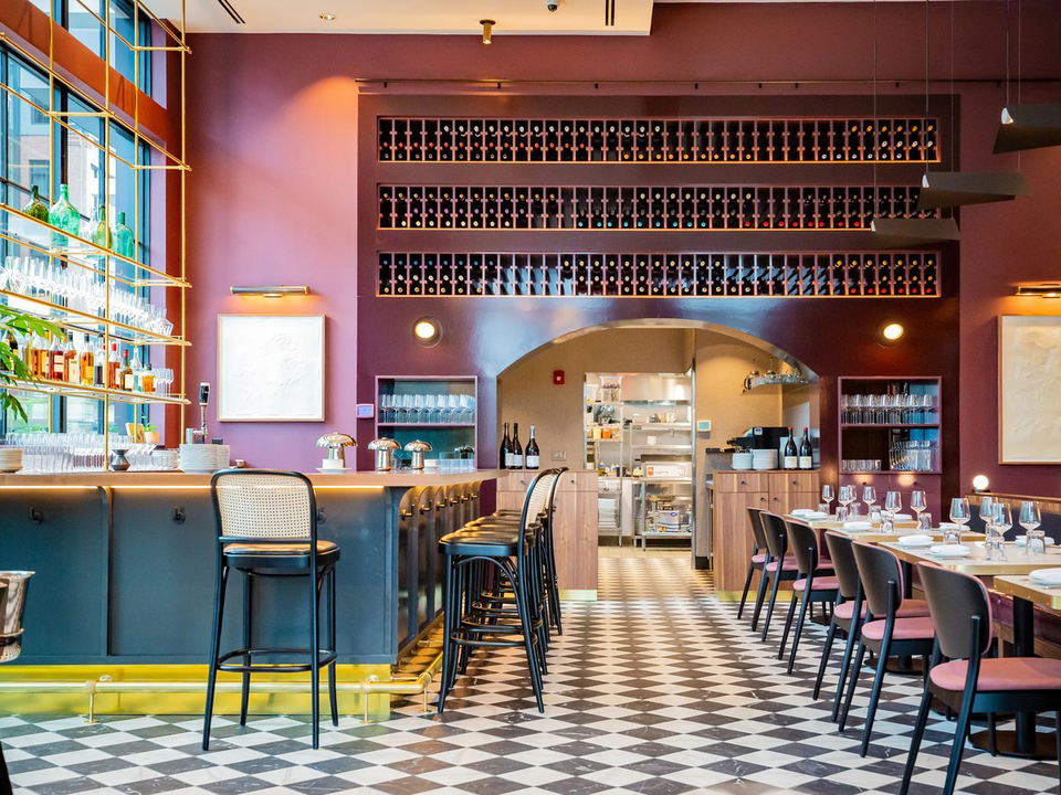 The interior of a restaurant with mauve-pink walls, a black-and-white checkered marble floor, a bar with gold shelving, and extensive wall-mounted