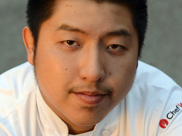 A close-up portrait of a young Asian male chef wearing a white Chef Works uniform jacket.