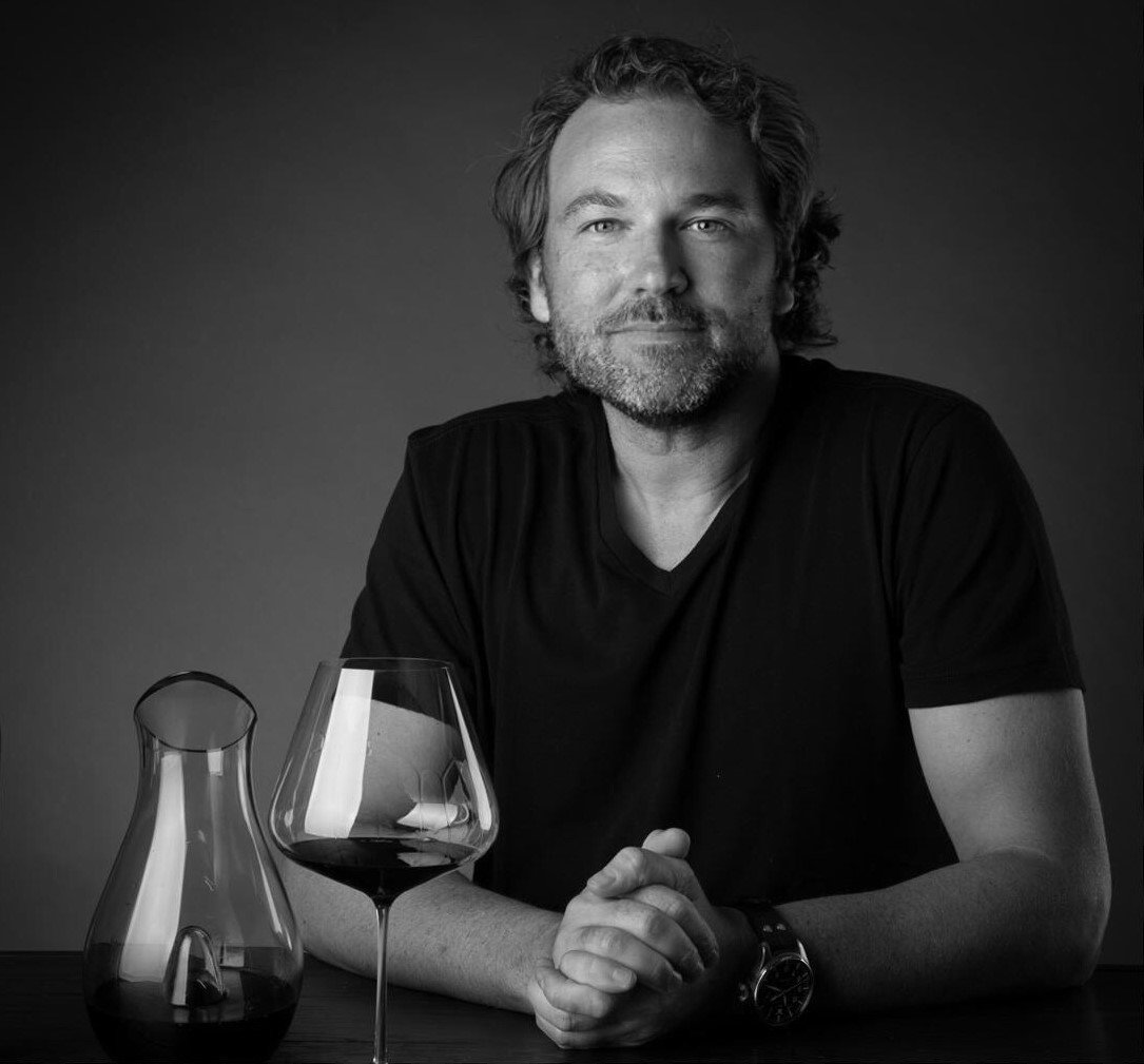 Professional black-and-white portrait of a man at a tasting table with wine decanter and glass