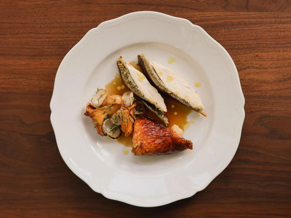 A plated dish featuring roasted chicken, grilled vegetables, and sliced fish or seafood with herbs.