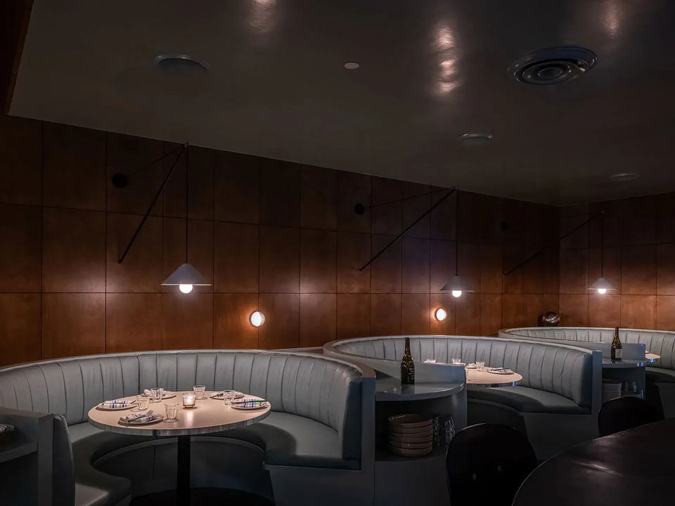 A dimly lit dining room at Bar Etoile features curved gray banquette booths, round tables, and warm copper-toned wall paneling.