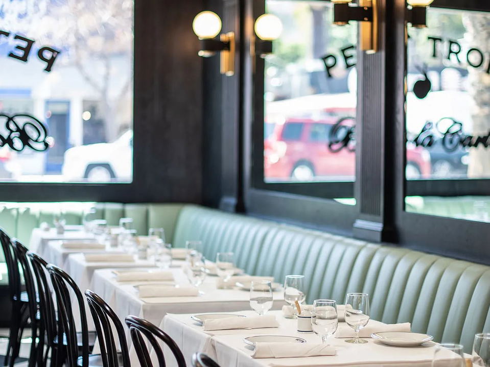 The interior of Petit Trois in Sherman Oaks, featuring mint-green banquette seating, white-tablecloth tables, and large windows with 'PETIT TROIS'