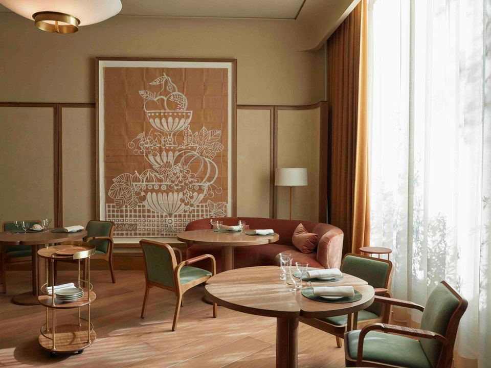 Quince's elegant dining room features round tables, green chairs, and a large fruit-themed artwork.