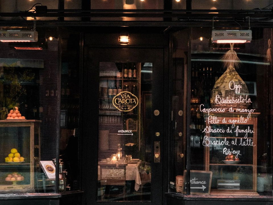 The exterior of Via Carota at 51 Grove Street, with a dark awning, string lights, and a menu of daily specials on the window.
