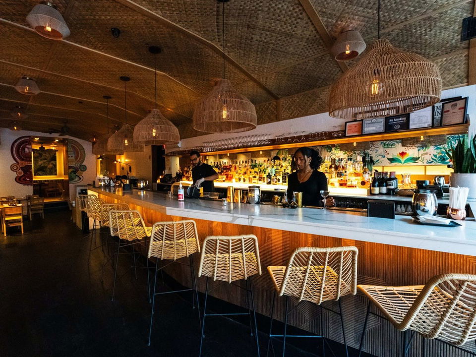Semma: A warmly lit bar with wicker pendant lights, rattan stools, and a well-stocked back bar.
