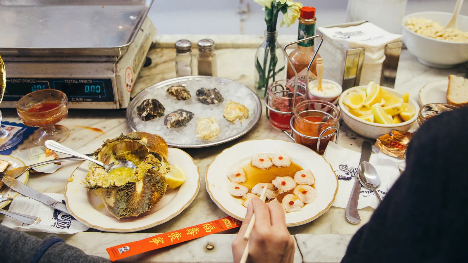 A marble counter at Swan Oyster Depot with oysters on ice, a Dungeness crab shell, shrimp cocktail, condiments, lemon wedges, and a scale.
