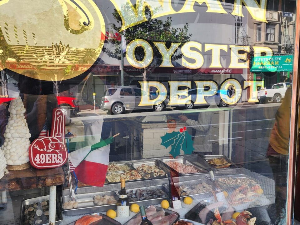 The storefront window of Swan Oyster Depot, displaying fresh seafood on ice, lemons, wine bottles, and a 49ers foam finger.