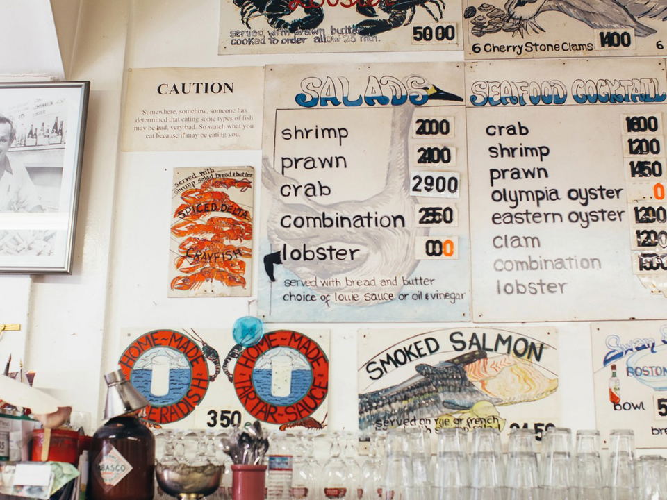 Handwritten menu boards at Swan Oyster Depot display various seafood options like shrimp, crab, and lobster, with prices listed.