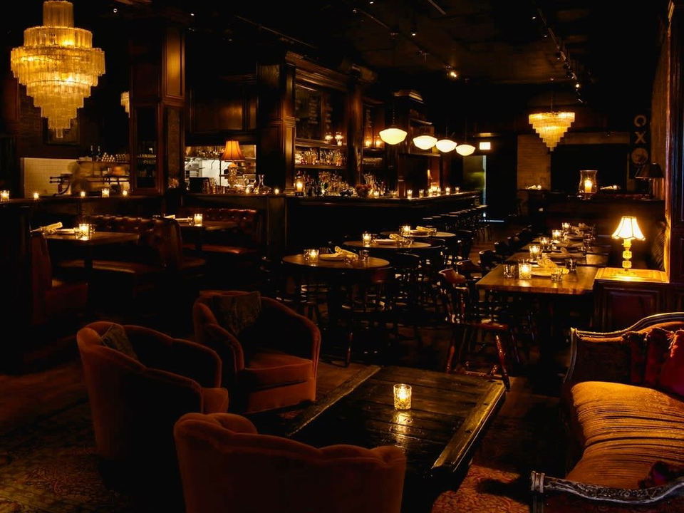 A dimly lit, opulent dining room at Gibsons Bar and Steakhouse, featuring dark wood paneling, tufted leather booths, velvet armchairs, and crystal