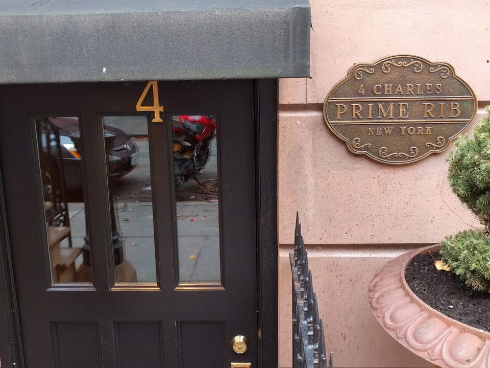 The exterior of 4 Charles Prime Rib, featuring a black door with a gold '4' and a bronze plaque reading '4 Charles Prime Rib New York'.