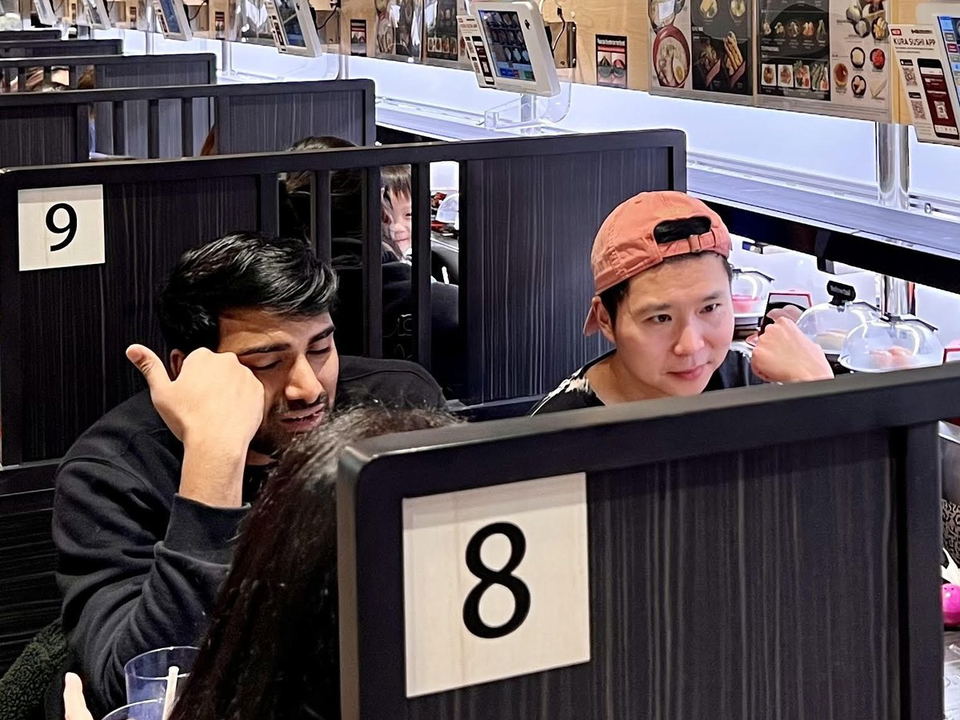 Interior of Kura Revolving Sushi Bar showing numbered booth seating, a conveyor belt sushi counter, Tetris x Kura branded signage and balloons, and